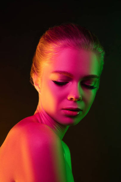 Portrait of female fashion model in neon light on dark studio background. - Zdjęcie, obraz
