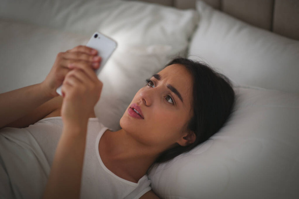 Emotional young woman with nomophobia using smartphone in bed at night. Insomnia concept - Fotó, kép