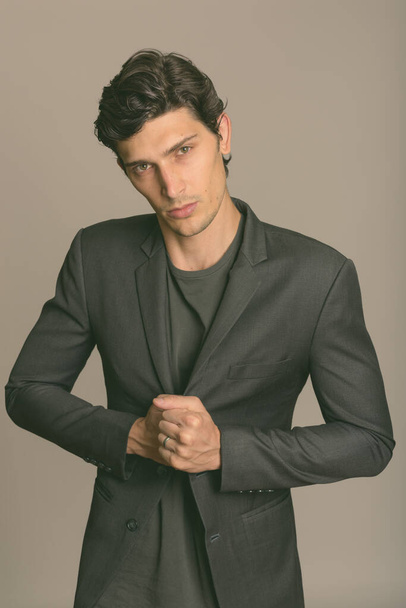 Studio shot of young handsome businessman holding jacket against gray background - Foto, Imagem