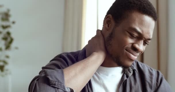 Portret van de jonge Afro-Amerikaanse zakenman student freelancer zittend op kantoor thuis tafel voelen pijn in de nek vermoeide expressie tijd om te rusten. Gemengde ras man die last heeft van pijn in de schouders - Video