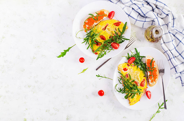 Omelet met tomaten, kaas, ham en broodje met rode cavier op bord. Frittata - Italiaanse omelet. Bovenaanzicht, bovenleiding, kopieerruimte - Foto, afbeelding