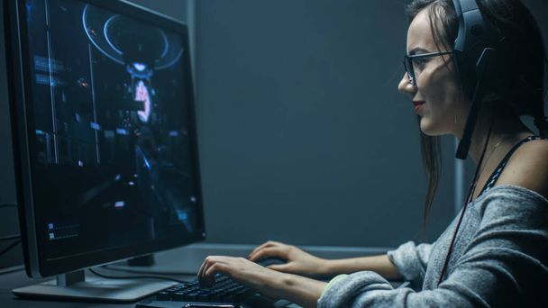Shot of the Beautiful Professional Gamer Girl Playing in First-Person Shooter Online Video Game on Her Personal Computer. Casual Cute Geek wearing Glasses and Talking into Headset. In the Basement - Foto, imagen