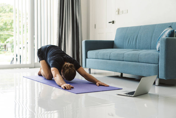 Sportlicher Mann macht Yoga, während er Online-Tutorial am Laptop anschaut - Foto, Bild