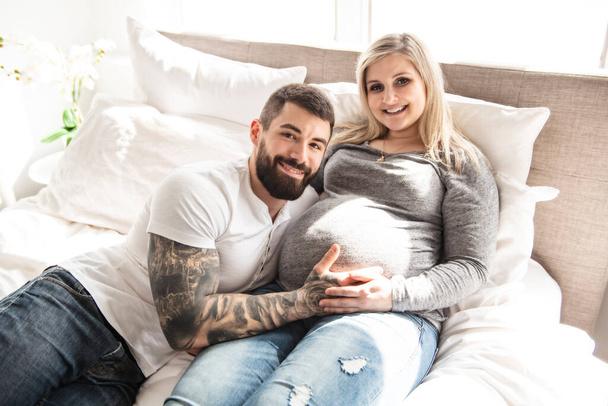 the man leaned against to the baby bump of his pregnant wife, who is lying on the bed - Фото, изображение