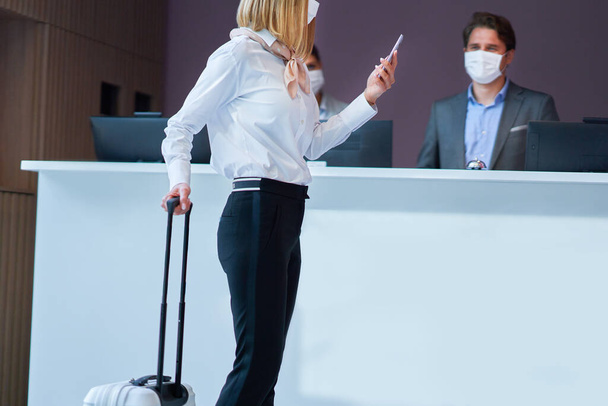 Geschäftsfrau mit Maske an der Rezeption eines Hotels beim Einchecken - Foto, Bild