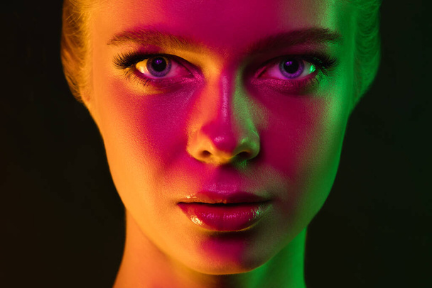 Portrait of female fashion model in neon light on dark studio background. - Foto, imagen