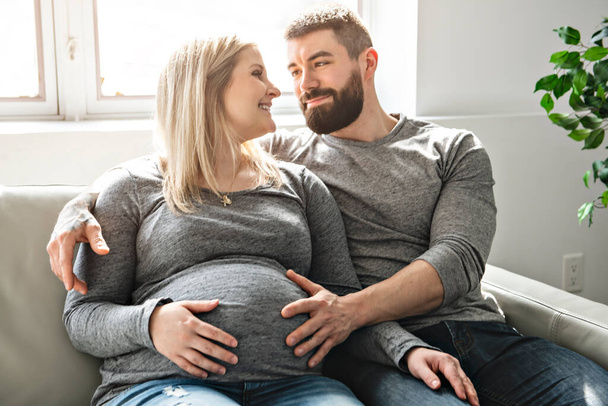 A man embracing happy pregnant woman sitting on couch - Foto, Imagem
