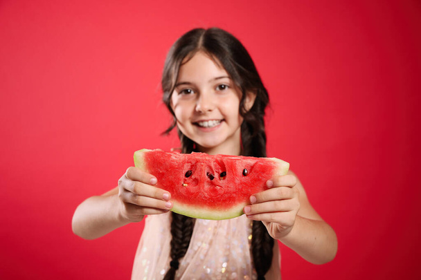 Cute little girl against red background, focus on hands with watermelon - Foto, imagen
