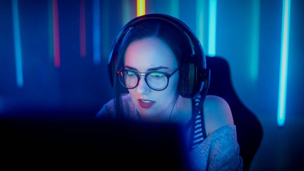 Beautiful Professional Gamer Girl Playing in Online Video Game on Her Personal Computer. Casual Cute Geek wearing Glasses and Talking into Microphone. Cyber Sport Internet Competition. - Фото, изображение