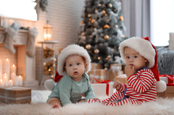 Cute children in Santa hats on floor in room with Christmas tree - Foto, Imagen