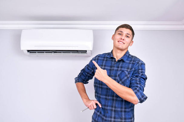 Joyful professional fixer installed indoor air conditioner, points finger and smiles, good service - Fotó, kép