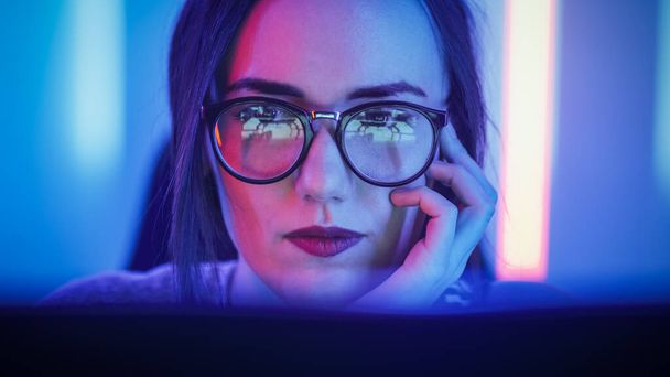 Portrait of the Beautiful Young Girl Sitting Before Computer Screen, Browsing in Internet, Playing Online Games, Streaming. Cute Girls Wearing Glasses in the Cool Retro Neon Lit Room. - Φωτογραφία, εικόνα