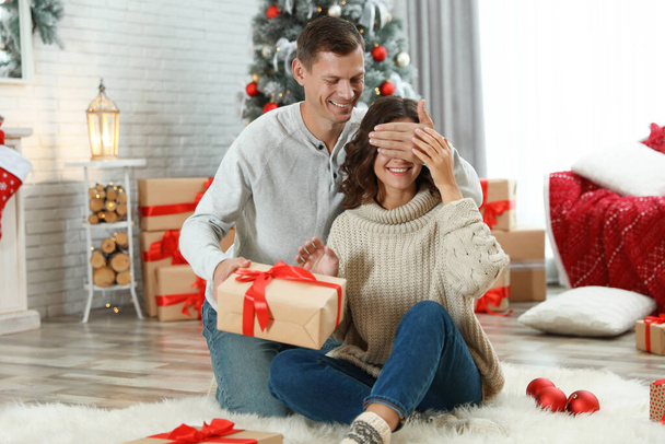 Ο άνθρωπος παρουσιάζει χριστουγεννιάτικο δώρο στην κοπέλα του στο σπίτι  - Φωτογραφία, εικόνα