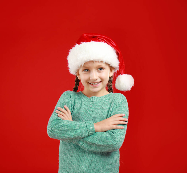 Happy little child in Santa hat on red background. Christmas celebration - Zdjęcie, obraz