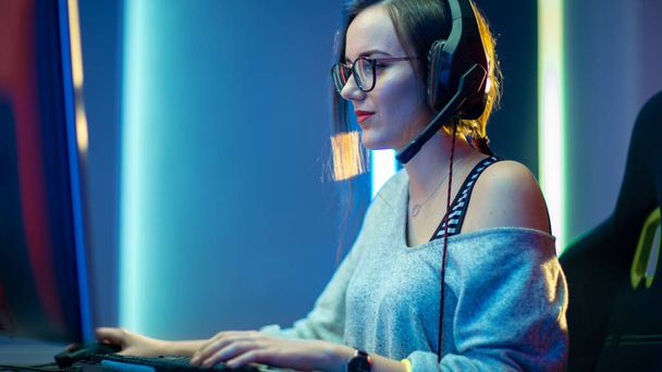 Beautiful Professional Gamer Girl Playing in First-Person Shooter Online Video Game on Her Personal Computer. Casual Cute Geek wearing Glasses and Smiling. Cyber e-Sport Internet Championship. - Foto, Imagem