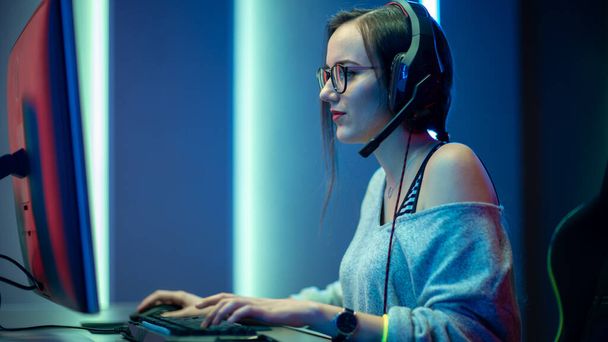 Beautiful Professional Gamer Girl Playing in First-Person Shooter Online Video Game on Her Personal Computer. Casual Cute Geek wearing Glasses and Smiling. Cyber e-Sport Internet Championship. - Foto, afbeelding