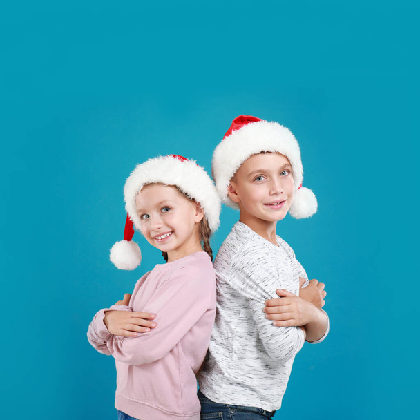 Happy little children in Santa hats on light blue background. Christmas celebration - 写真・画像