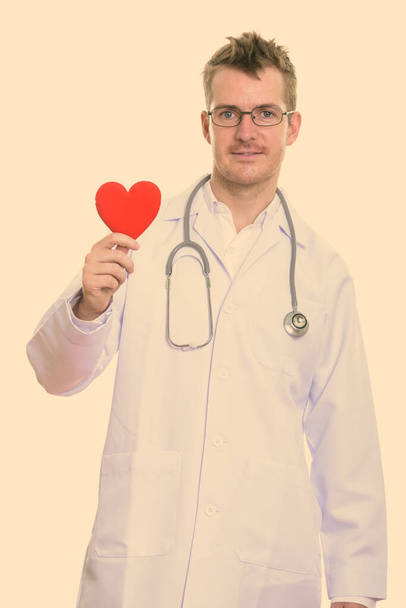 Στούντιο πλάνο του ευτυχισμένος άνθρωπος γιατρός χαμογελά, ενώ κρατώντας κόκκινη καρδιά - Φωτογραφία, εικόνα