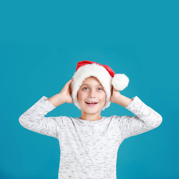 Happy little child in Santa hat on light blue background. Christmas celebration - Fotó, kép