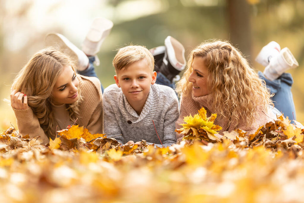 Blonde family of mother, teenage girl and boy lie down on a foliage enjoying good times together. - 写真・画像