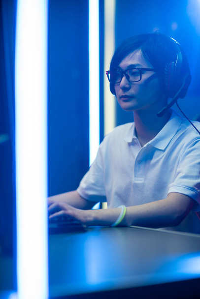 Professional Gamer Playing Online Video Game on His Personal Computer. Hes Talking with His Team Through Headset. Room Lit by Neon Lights in Retro Arcade Style. Vertical Shot. - Foto, imagen