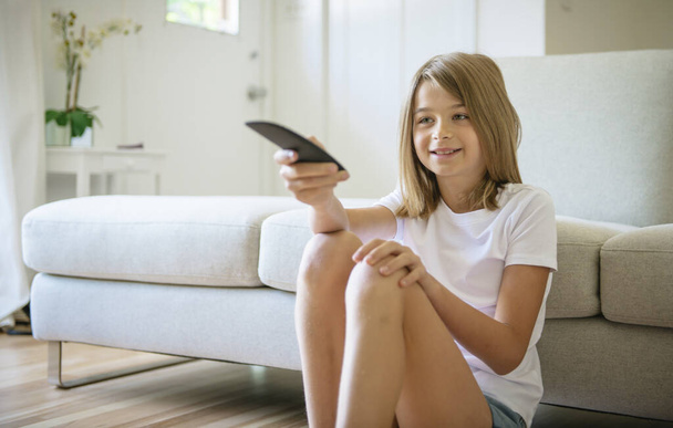 A girl holding remote control and watching TV show - 写真・画像