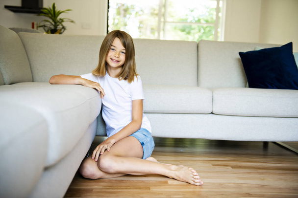 A Cute girl sitting on the sofa and watching TV. The child is resting at home. - Foto, Imagem