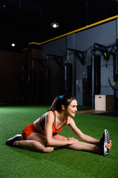 lächelnde Sportlerin mit Turnschuhen beim Stretching im Sportzentrum - Foto, Bild