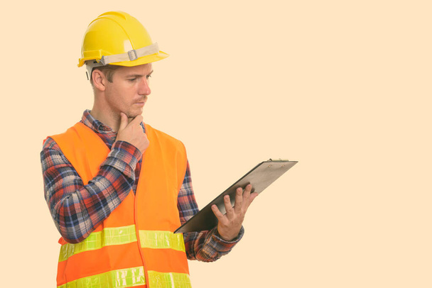 Studioaufnahme eines Bauarbeiters, der auf Klemmbrett liest, während er denkt - Foto, Bild