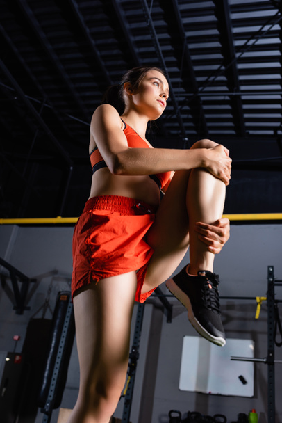low angle view of sportswoman in shorts stretching leg in sports center - Foto, Imagen