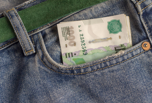 У кишені блакитних джинсів стоїть паперовий тисячний рахунок. Гроші, бюджет, доходи, витрати, фінанси та економіка
. - Фото, зображення