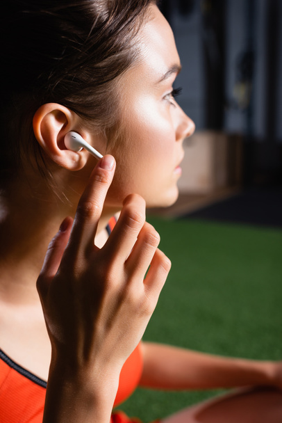 sportswoman looking away while touching wireless earphone in gym - Foto, Imagem