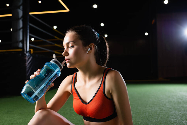 junge Sportlerin trinkt in Turnhalle aus Sportflasche - Foto, Bild
