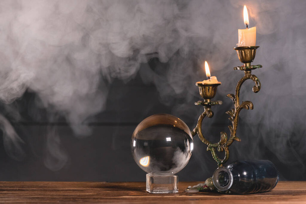 Crystal ball and burning candle on the table in the smoke. - Foto, imagen
