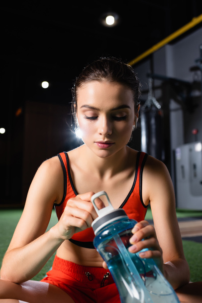 thirsty sportswoman opening sports bottle in gym - Fotó, kép
