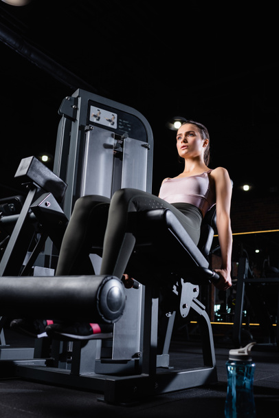 athletic sportswoman doing leg extension exercise on training machine - Foto, afbeelding