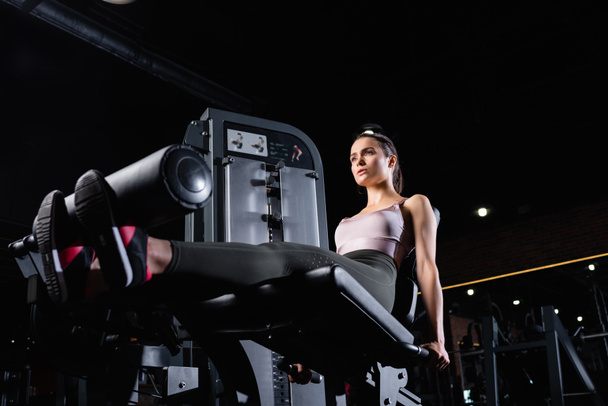 vue à faible angle de la formation sportive sur la machine d'extension de jambe dans la salle de gym - Photo, image
