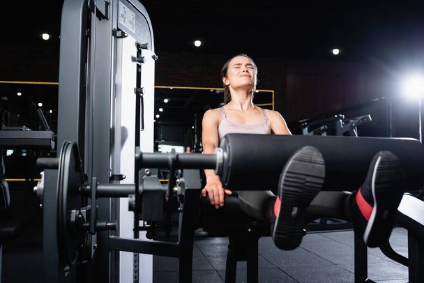 napjatá sportovkyně pracuje na prodlužovacím stroji nohou v tělocvičně - Fotografie, Obrázek