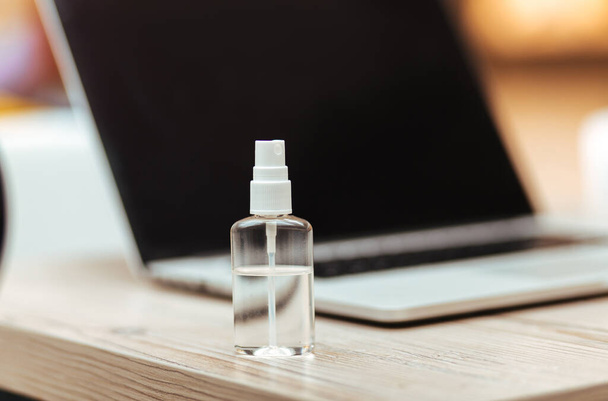 image of an antiseptic spray next to a laptop on the table. - Foto, Imagem
