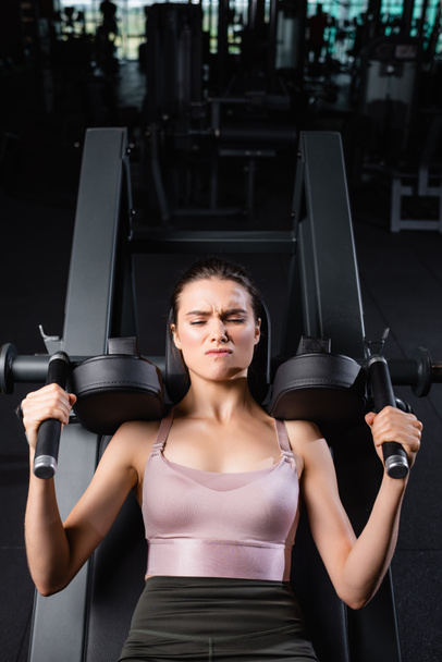 top view of sportswoman with closed eyes training on arms extension machine in gym - 写真・画像