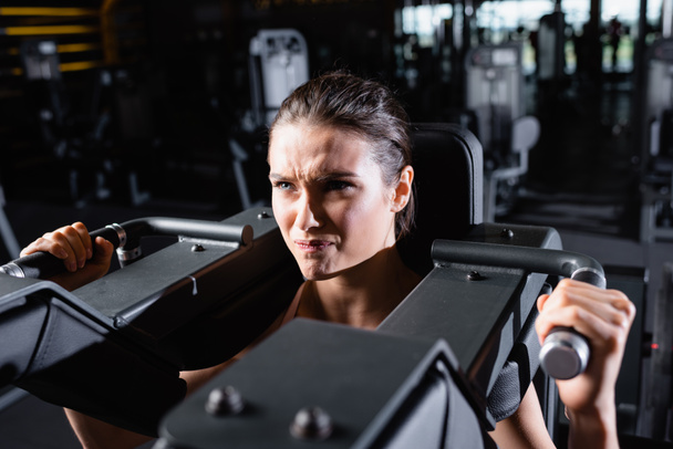 tense sportswoman working out on arms extension machine in gym - Fotó, kép