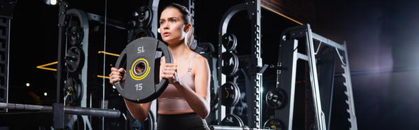 athletic sportswoman working out with weight disk in sports center, banner - Photo, Image