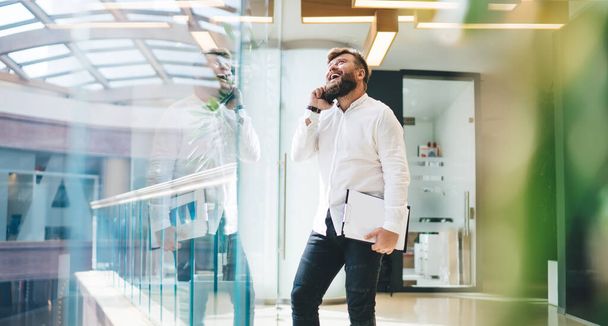Cheerful caucasian funny male employee in office talking on mobile phone laughing on break in office, 20s overjoyed caucasian man excited with business success news making smartphone call - Фото, зображення