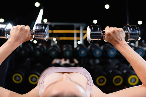 sportswoman exercising with dumbbells in lying position on blurred foreground - 写真・画像