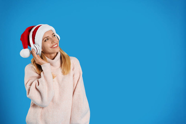 Happy woman with headphones on blue background, space for text. Christmas music - Fotoğraf, Görsel