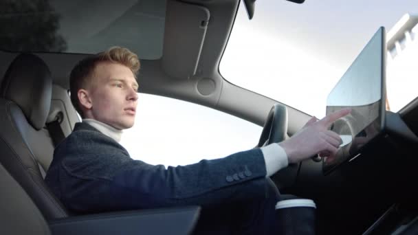 Egy fiatal, sikeres férfi portréja egy modern sportautó belsejében. A férfi egy érintőszámítógépet használ a kocsiban. Egy fiatal srác, szőke öltönyben. - Felvétel, videó
