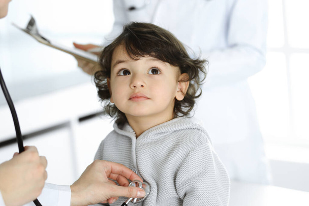 Kobieta-lekarz badający dziecko stetoskopem. Słodki arabski maluch na wizycie u lekarza. Koncepcja medycyny - Zdjęcie, obraz