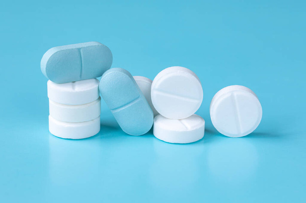 Witte en blauwe tabletten of pillen, of medicijnen of drugs. Een close-up. Selectieve focus. Farmacie, geneeskunde, medisch behandelingsconcept. - Foto, afbeelding