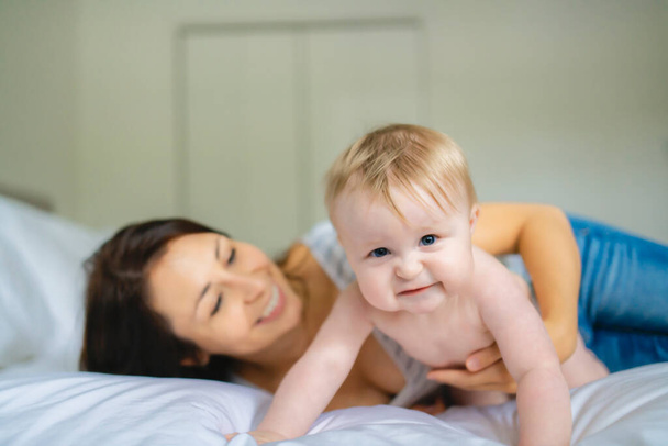 Mother and child on a white bed playing in sunny bedroom - Foto, imagen