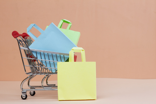 Small metal trolley and colored bags on a pink background. The concept of sales, online shopping, discounts. - Foto, Bild